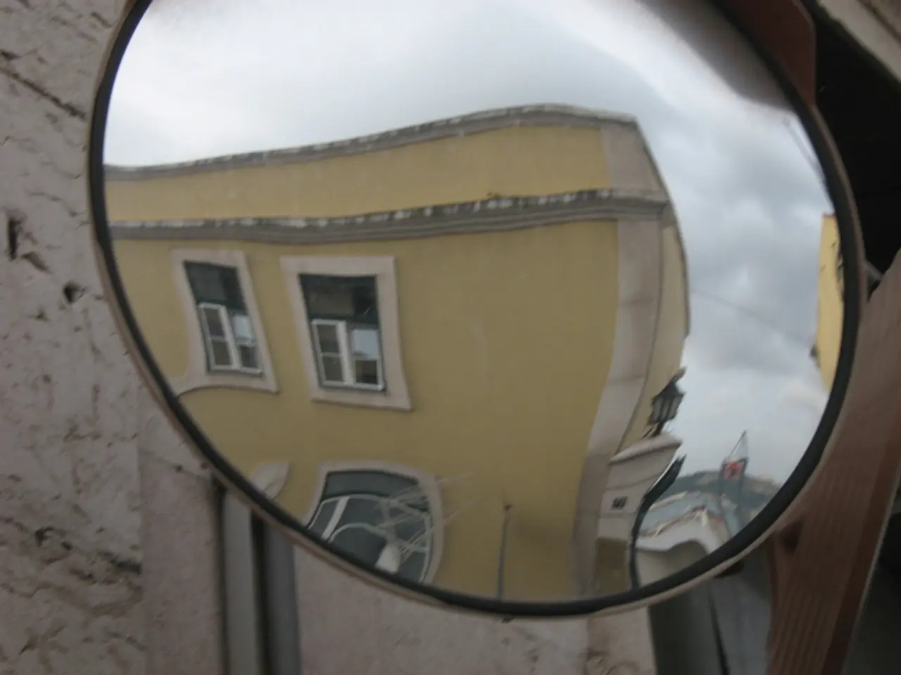 In this image there is a reflection of buildings, light and sky on the road safety mirror, and in...