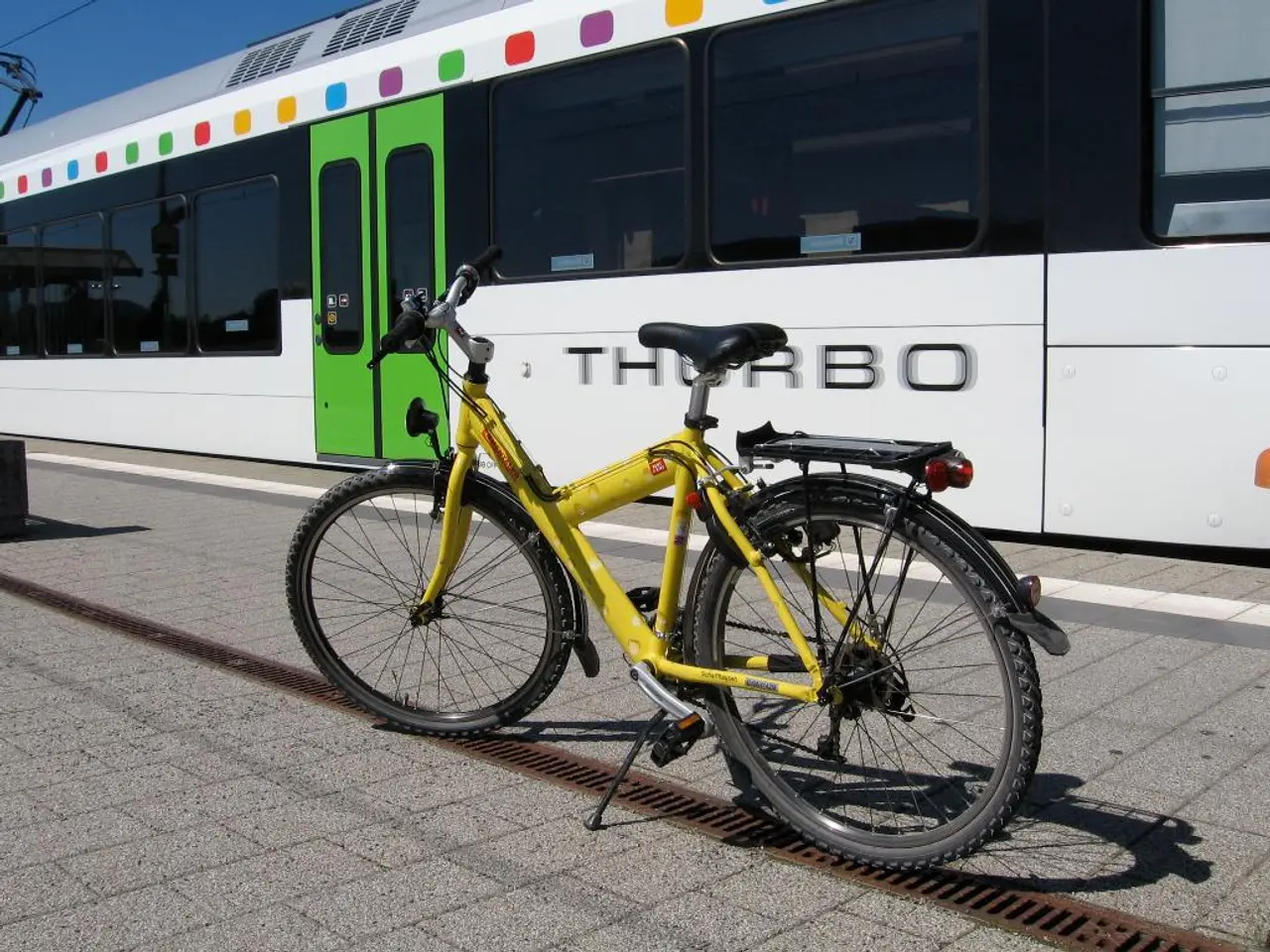 In this image we can see a locomotive on the track, bicycle on the floor, electric cables and sky.