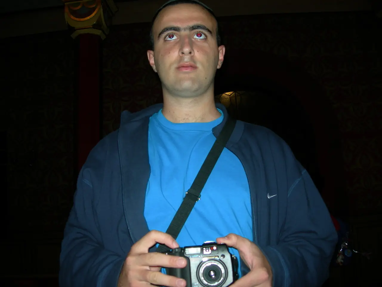 In this picture a man is standing and holding the camera with both hands and he is wearing a bank