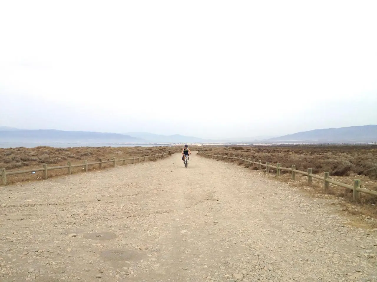 There is a plain road, a person is moving on a vehicle on the road, there is a fencing on the...