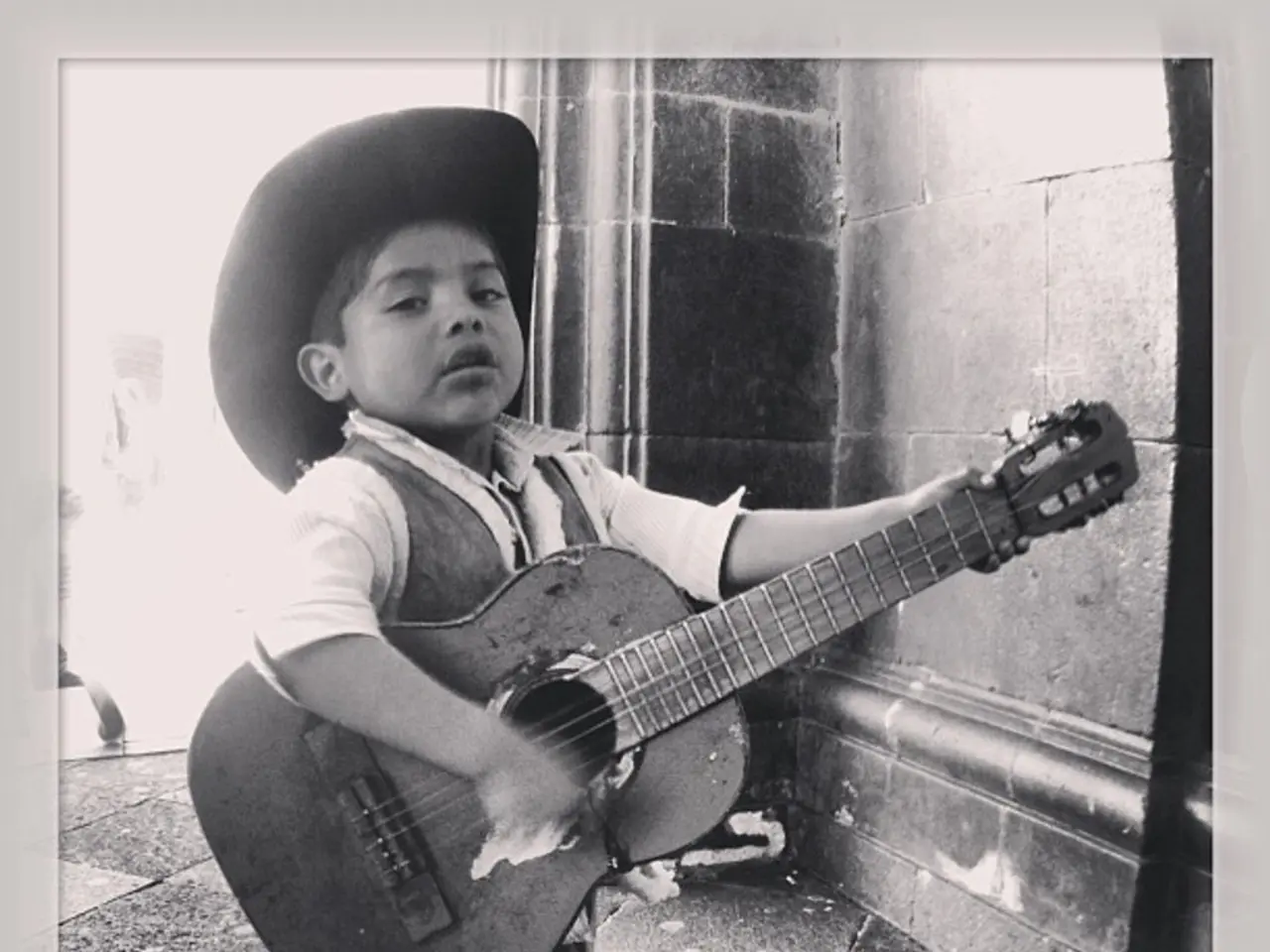 This is a black and white pic. Here we can see a boy is standing on the floor and holding a guitar...