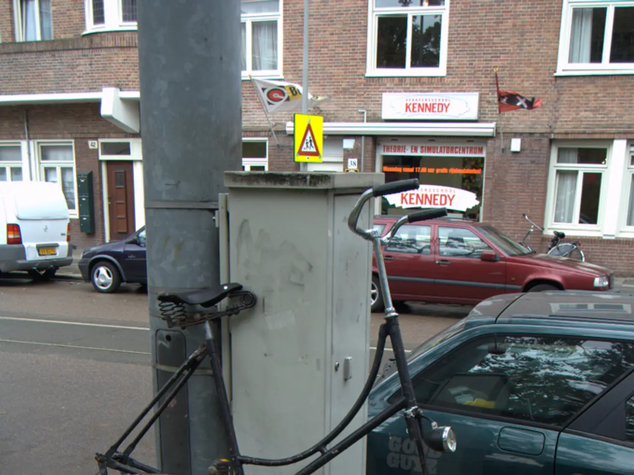 In this image I can see a bicycle. There are poles, name boards, vehicles, buildings, windows,...