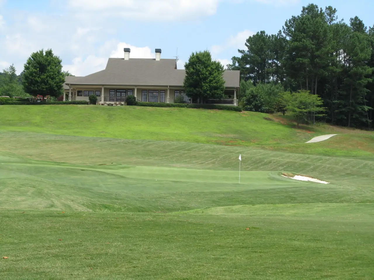 In this image there is a golf court , in the background there is a house, trees and a sky.