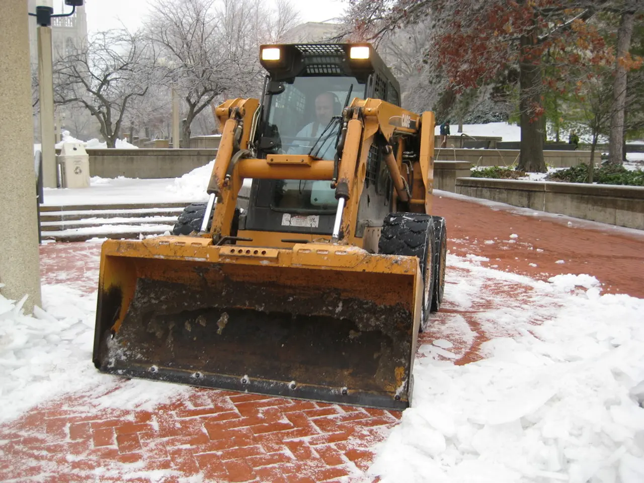 There is a man inside a vehicle and we can see snow. In the background we can see wall,trees,plants...