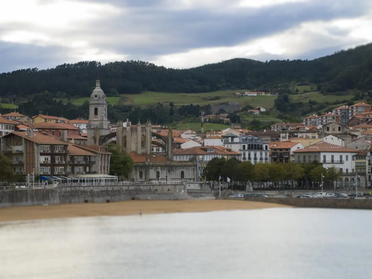 In this image I can see number of buildings, number of trees, clouds, the sky, number of vehicles...