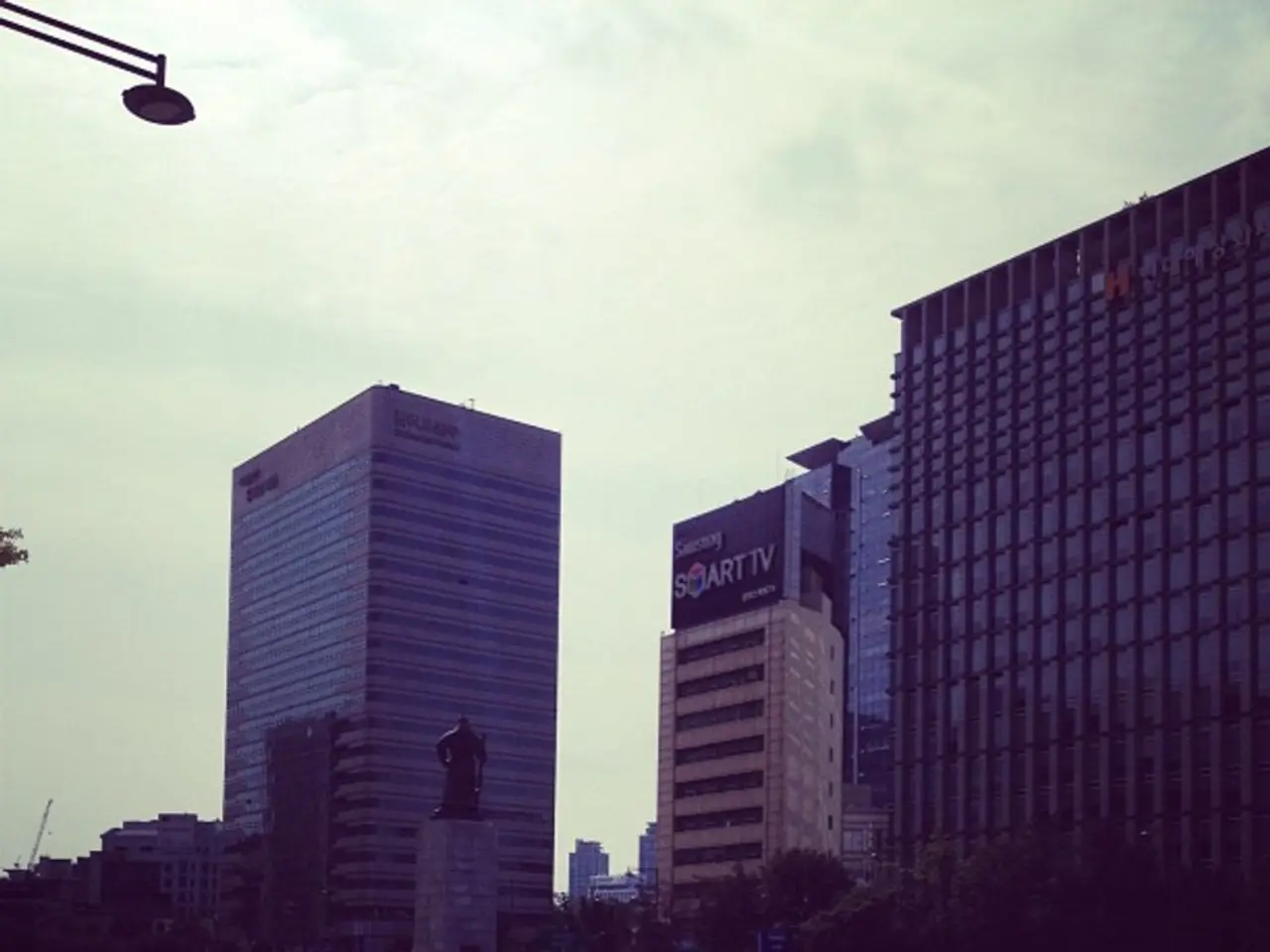 In this image there are cars passing on the road, beside the cars there is a fountain, beside the...