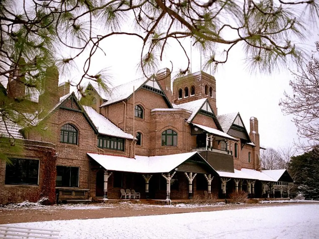 There is a building with windows, pillars and chairs. On the right there is a bench and a branch....
