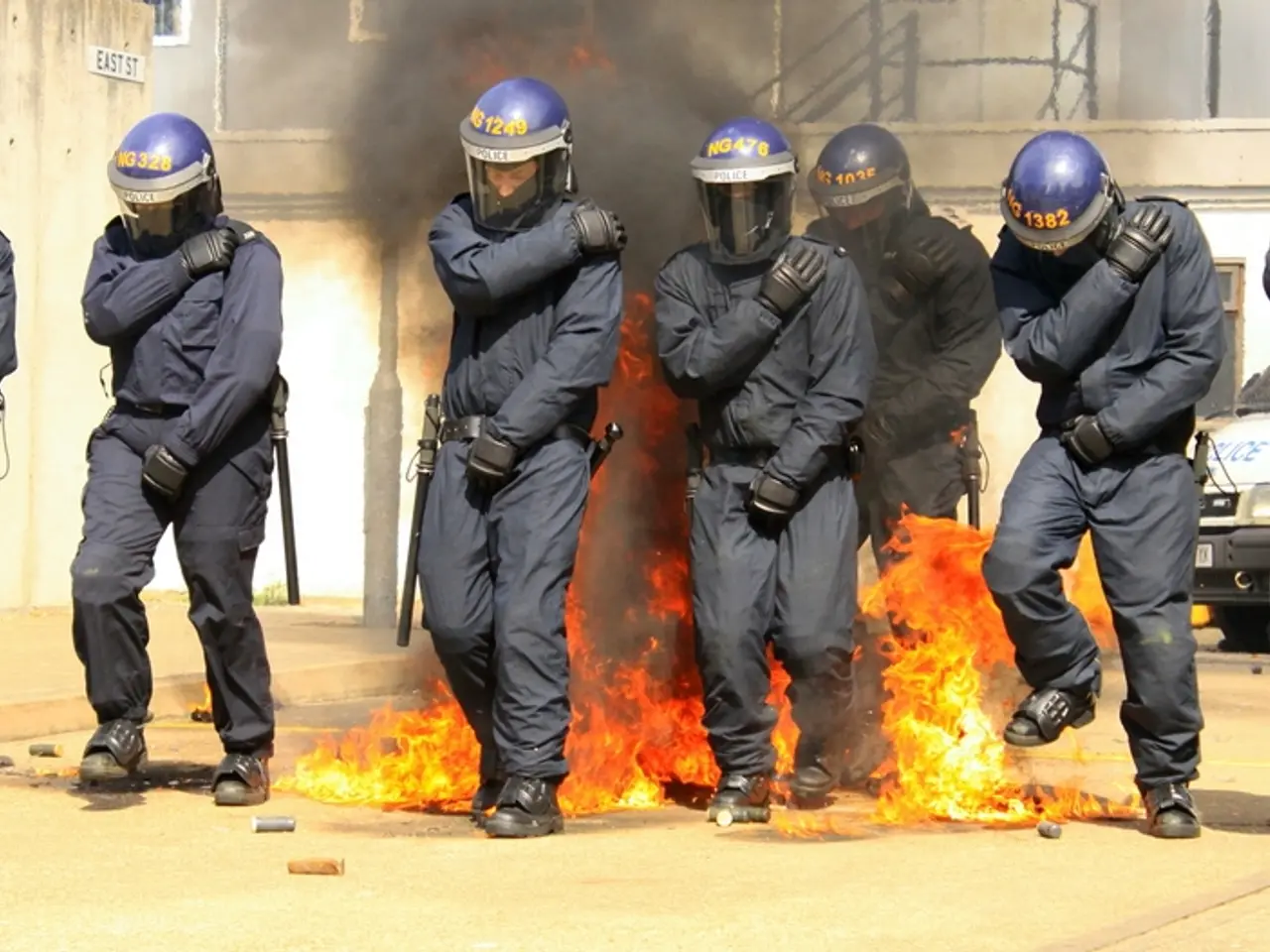 In this image there are people wearing helmets. Behind them there is a fire. There are a few...