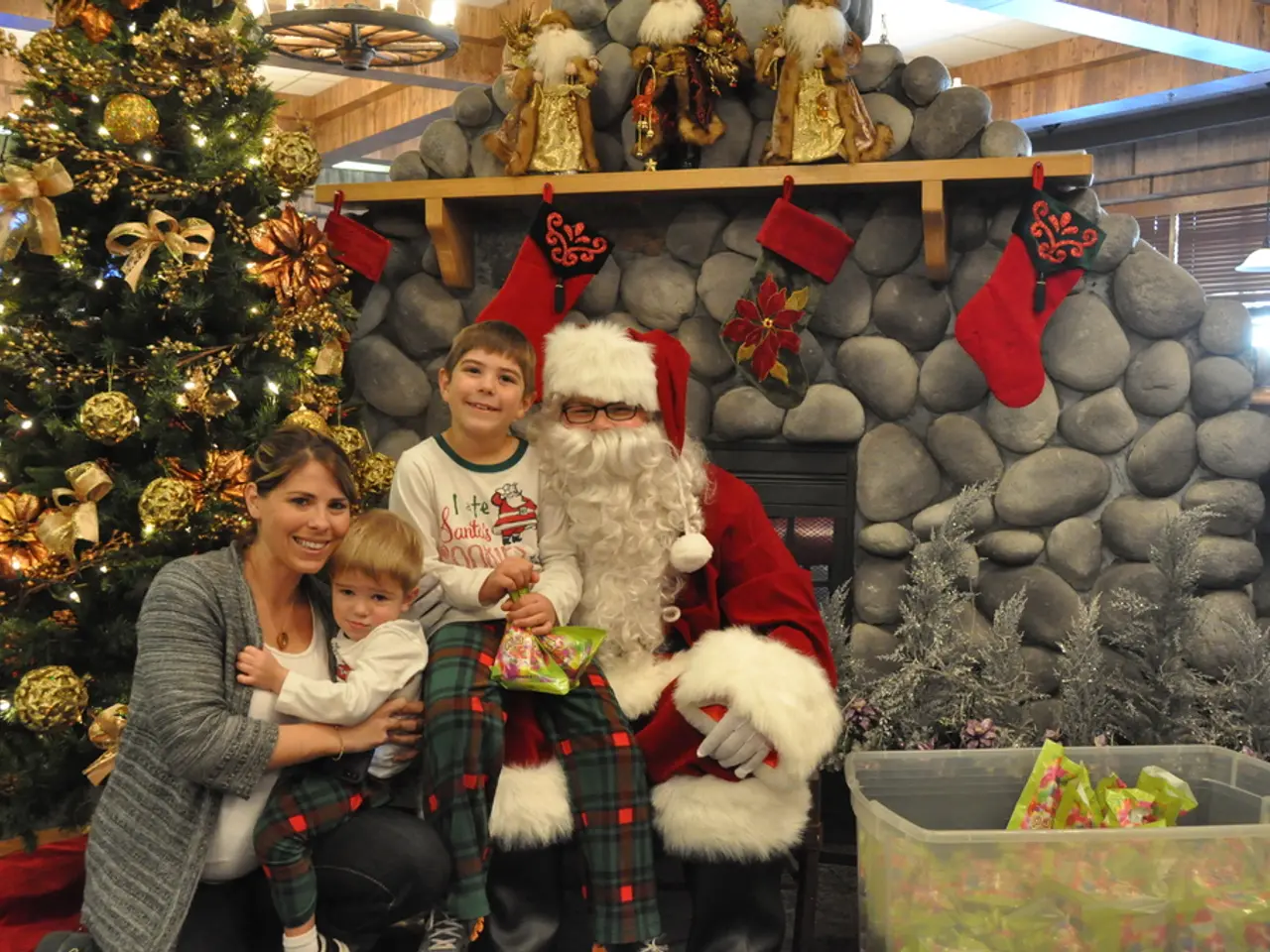 There is a lady, children and a man in santa claus dress. Man is wearing specs and gloves. Boy is...