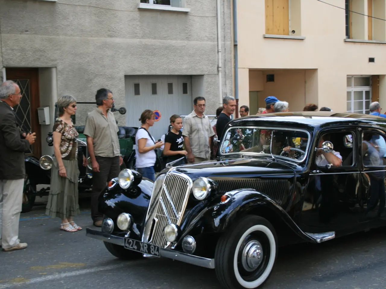 It's a car on the road. In the left side there are people standing behind them there are buildings.