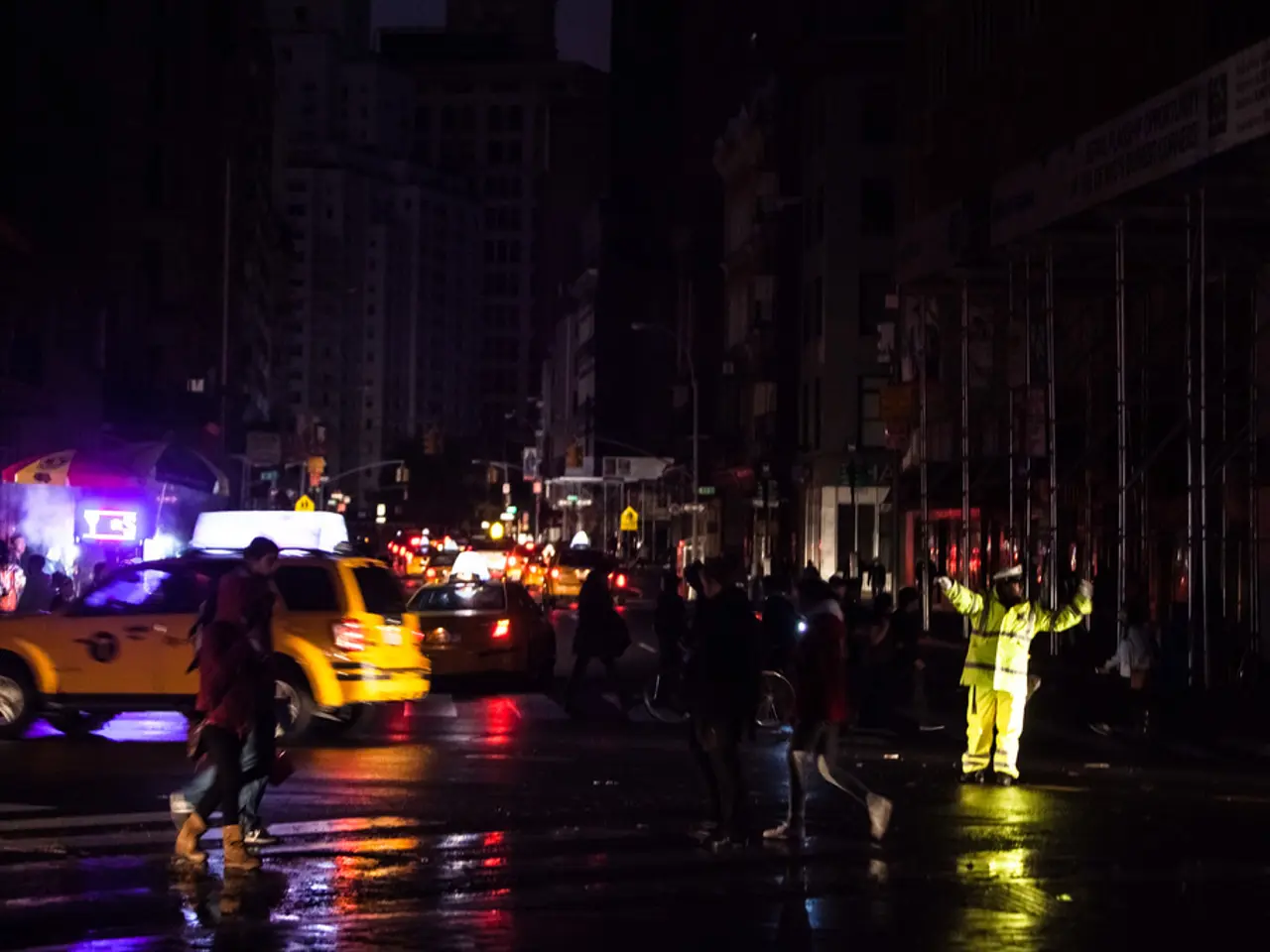 In the picture we can see a night view of the road with some people are standing and some cars and...