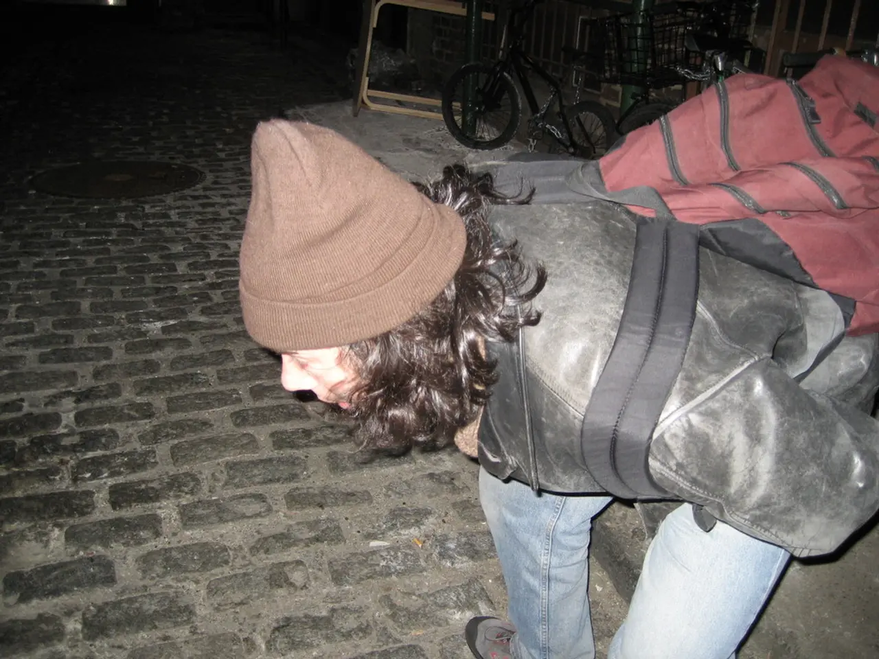 In this image we can see a person in a black jacket and in blue jeans carrying a red color of bag....