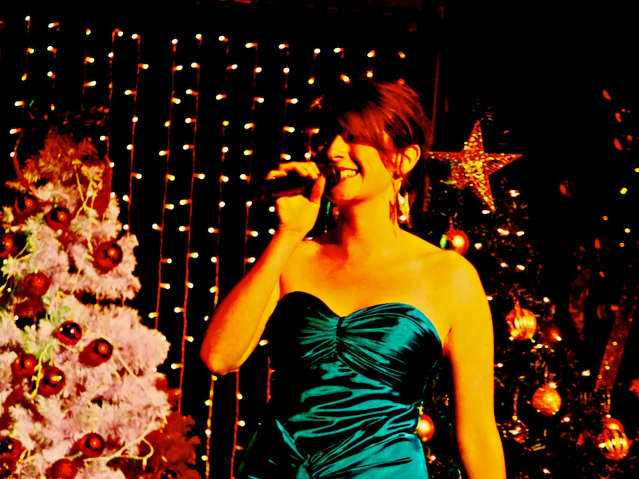 In the center of the image we can see a lady standing and holding a mic in her hand. In the...