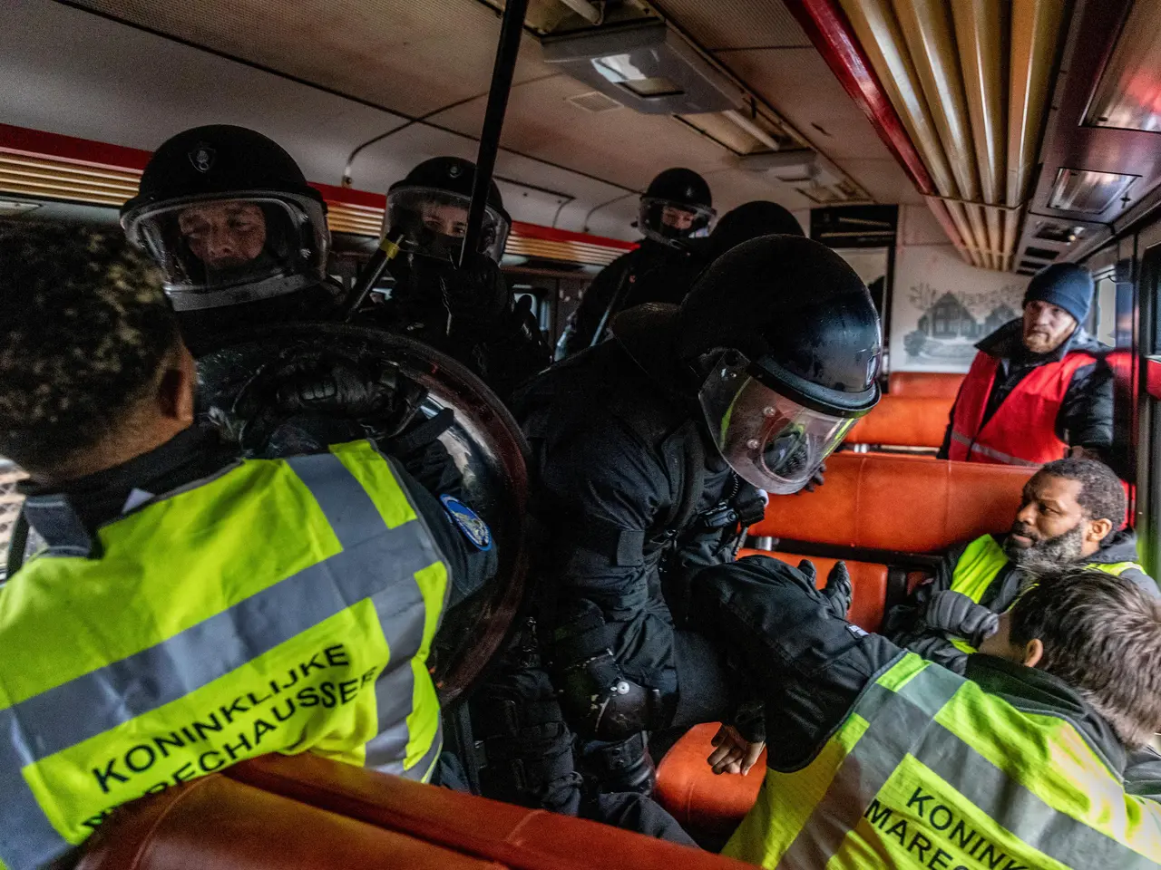 The image shows a group of police officers in riot gear on a bus, with some of them wearing helmets...