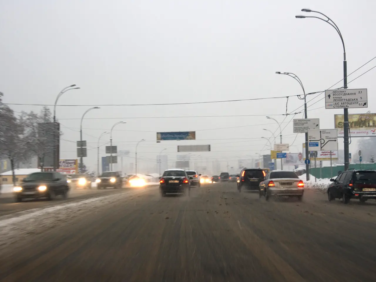 The image shows a city street filled with lots of traffic on a snowy day. We can see vehicles...