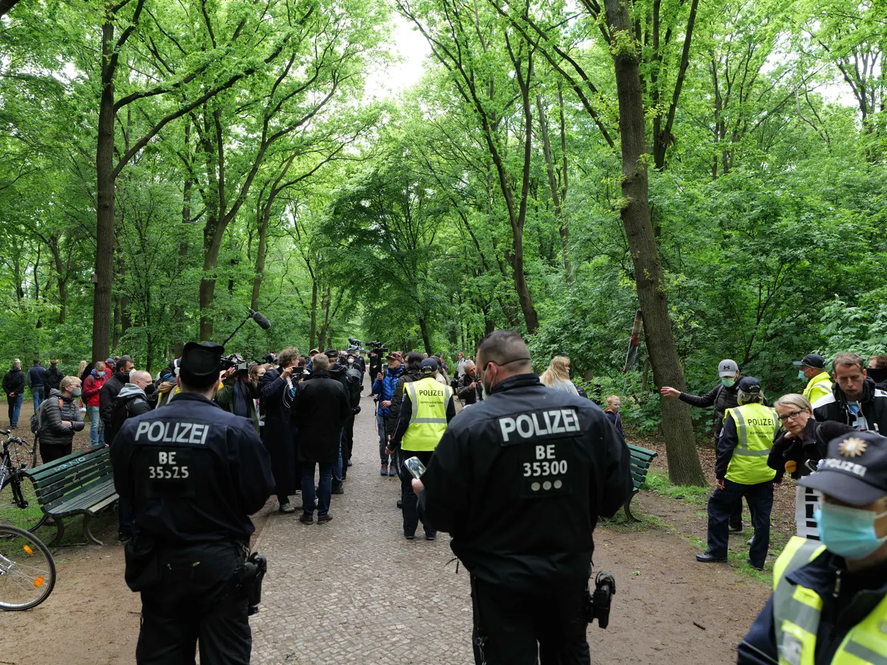 The image shows a group of police officers standing in front of a crowd of people, some of whom are...