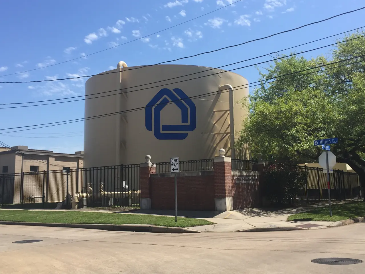 The image shows a large water tank sitting on the side of a road, surrounded by a fence, grass,...
