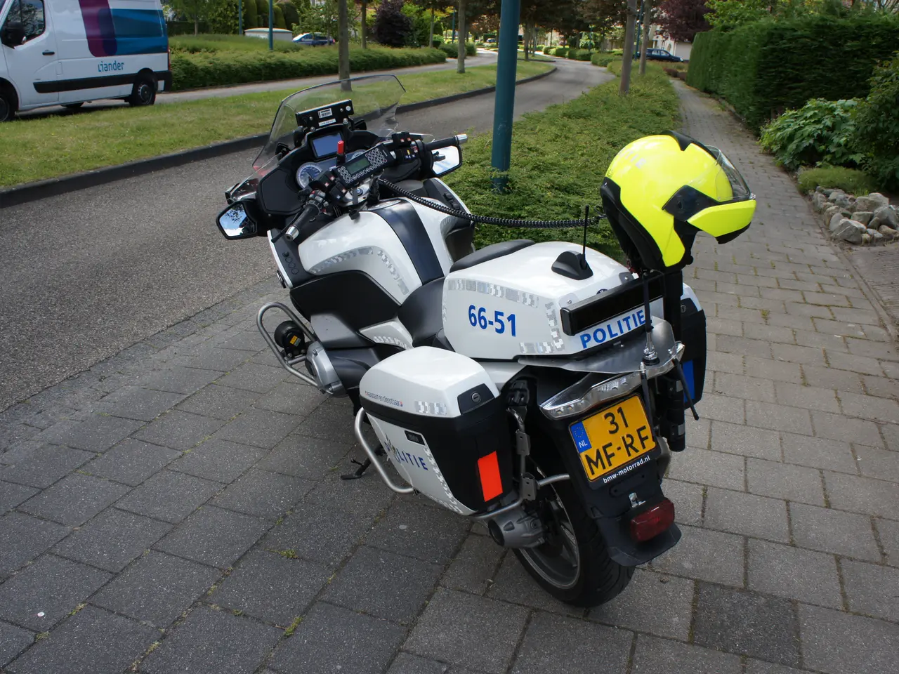 The image shows a police motorcycle parked on the side of the road, with a helmet placed on the...