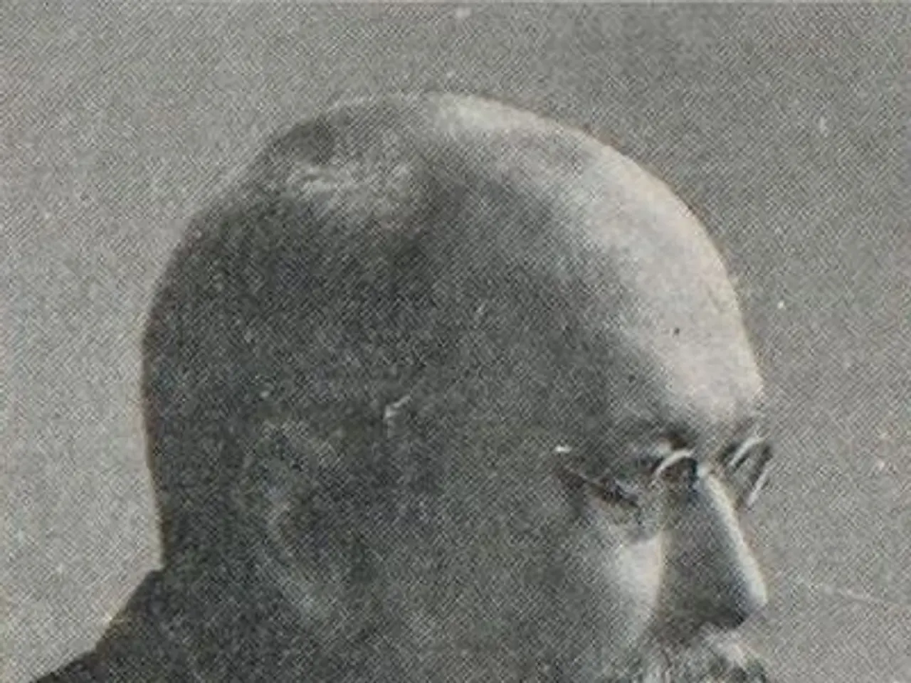 The image shows an old black and white photo of a man with a beard wearing a suit and spectacles....