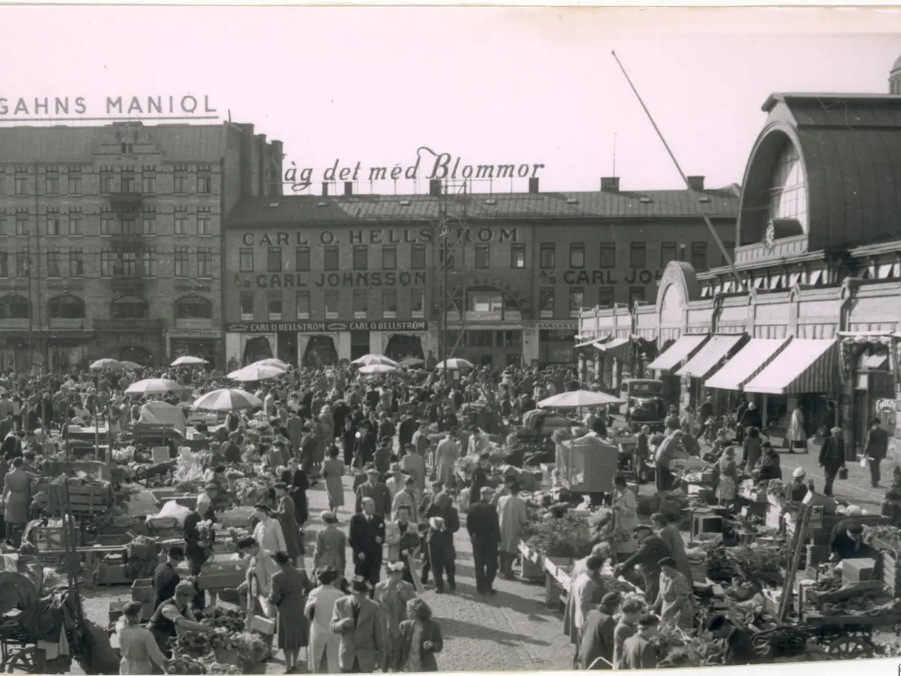 The image shows an old black and white photo of a bustling market in Berlin, Germany. There are...