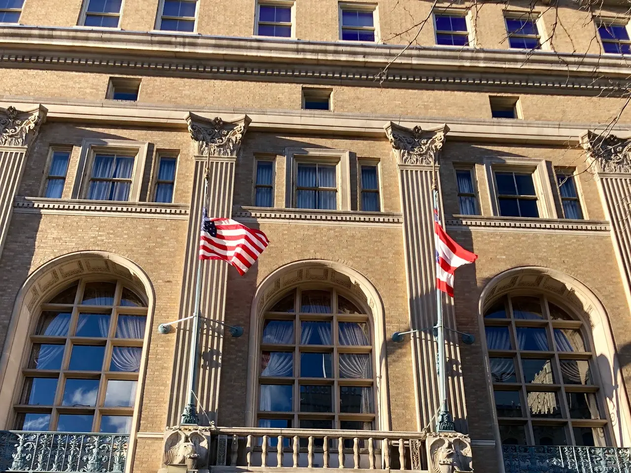 The image shows a large building with glass windows, doors, pillars, railings, lights, boards with...