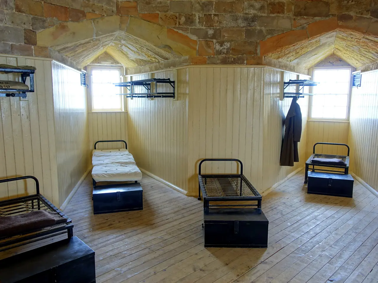 The image shows a room with wooden floors and a brick wall, containing a few beds with blankets and...
