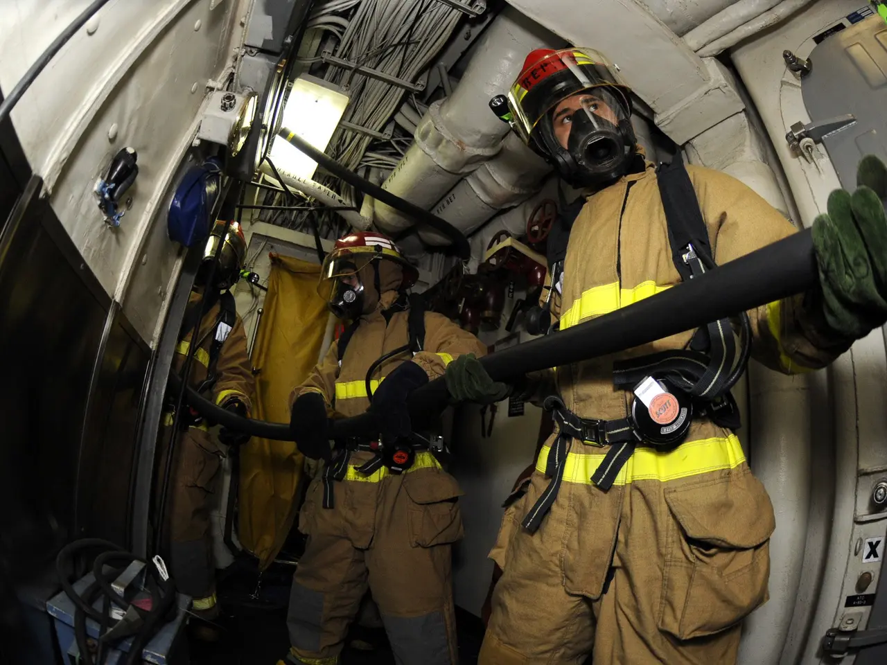 The image shows a group of firefighters wearing helmets and gloves, holding a hose in the back of a...