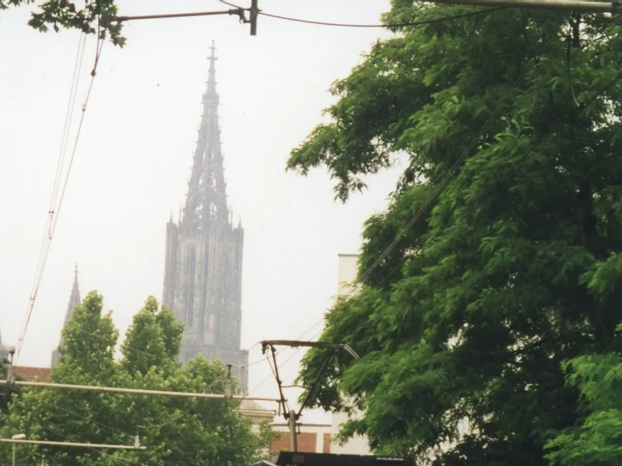 The image shows a red and white train traveling down tracks next to a tall building, with a person...