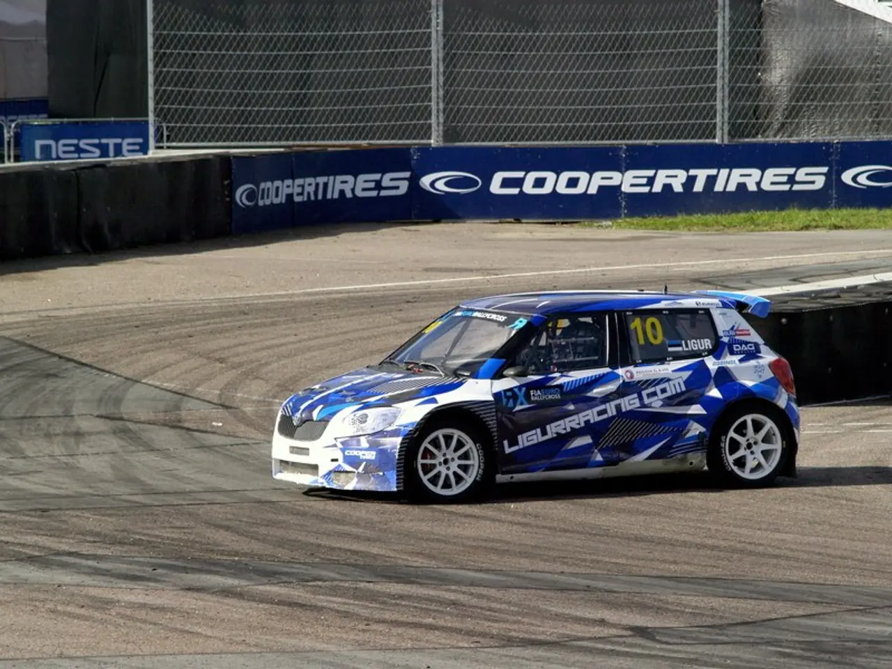 The image shows a blue and white car driving down a race track, with text and numbers on the car....