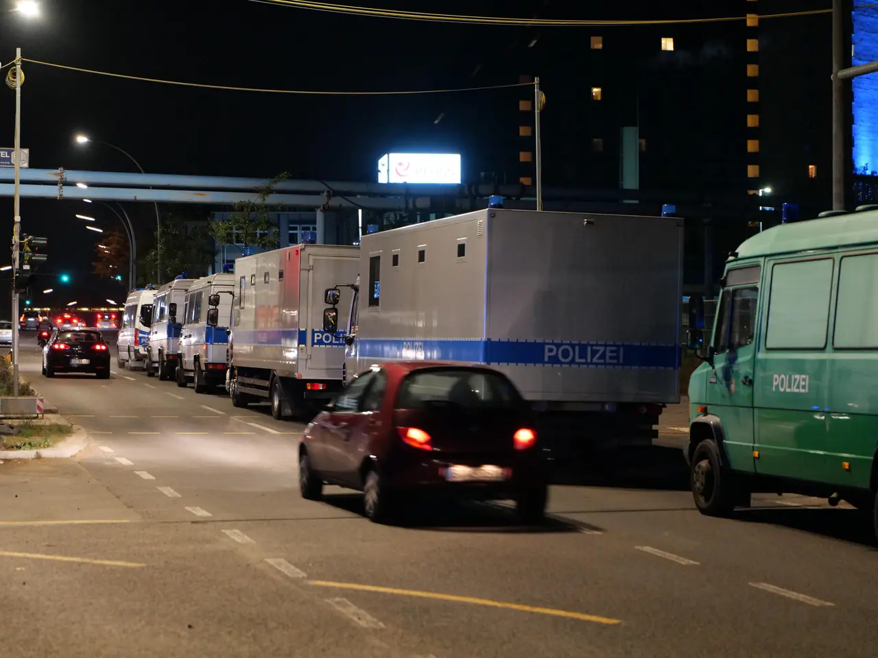 The image shows a long line of police cars and trucks parked on the side of a street at night. We...
