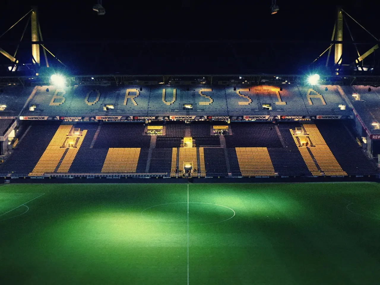 The image shows a soccer field at night with a lot of lights illuminating the stadium. The ground...