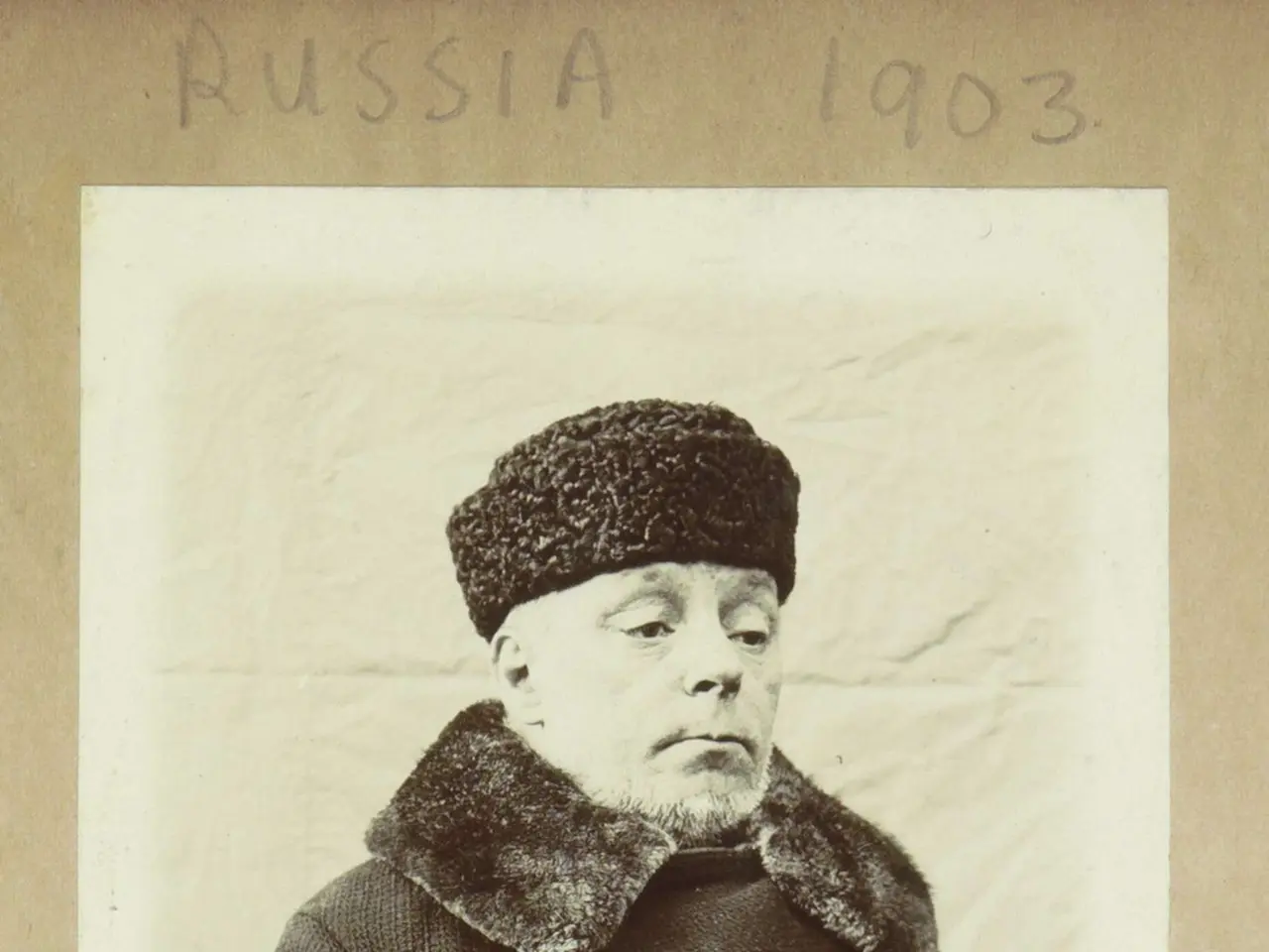 The image shows an old black and white photo of a man wearing a fur coat and a cap. The man is...
