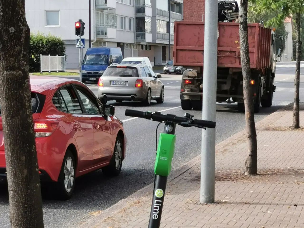 The image shows an electric scooter parked on the side of a street next to a tree. There are...
