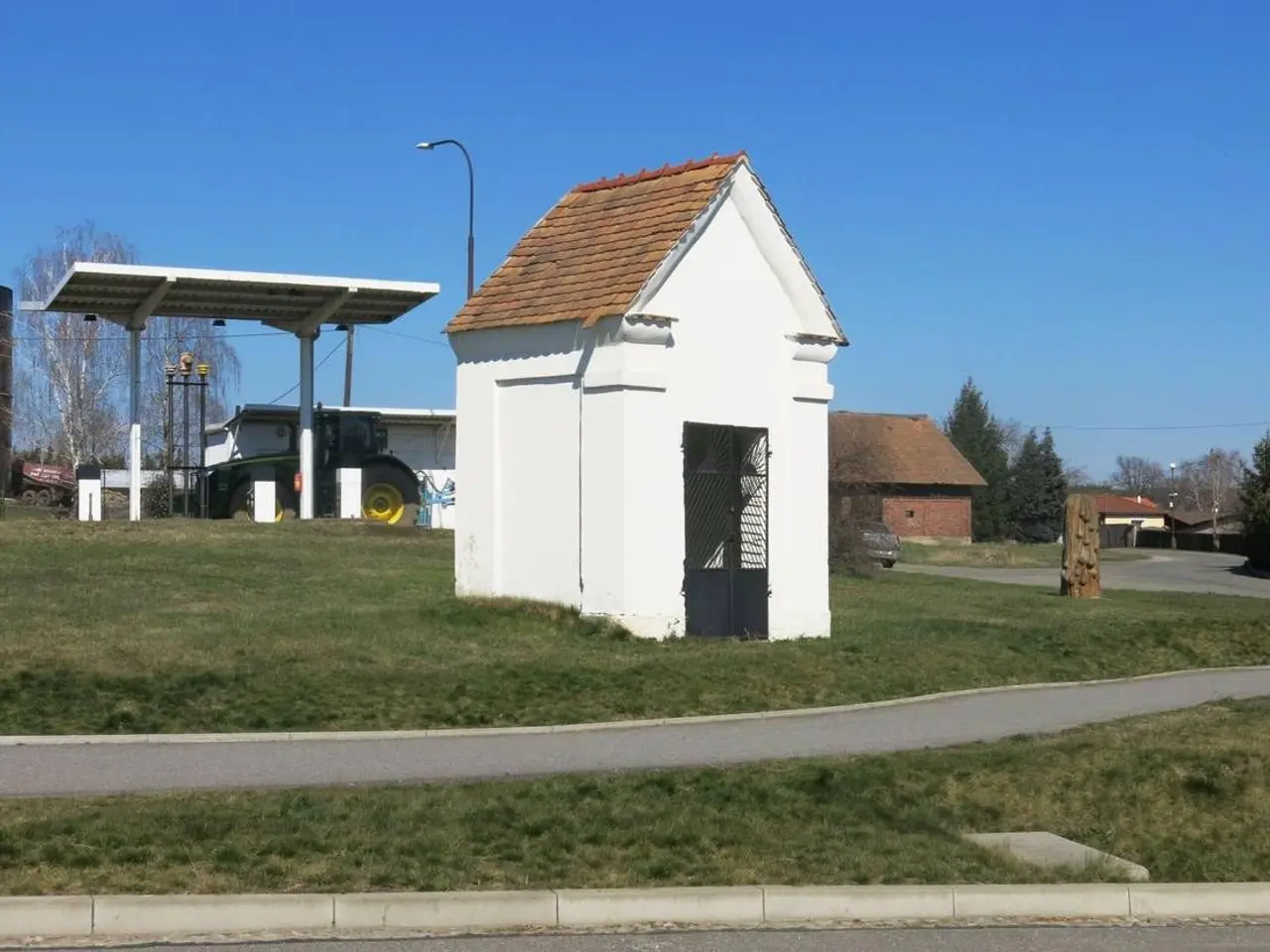 The image shows a small white building with a red roof sitting on the side of a road surrounded by...
