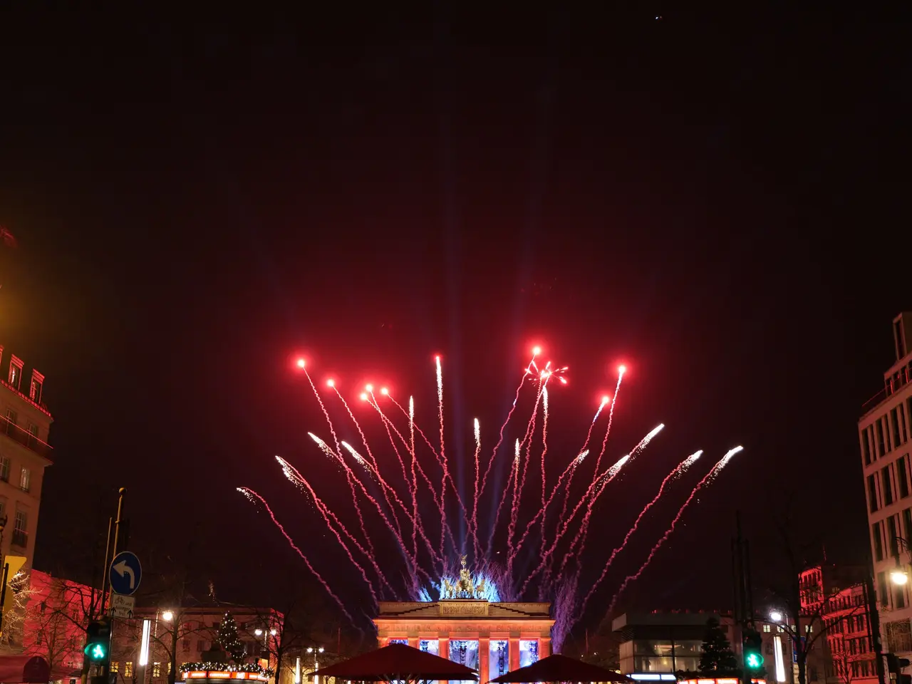 The image shows a city street filled with lots of buildings, trees, light poles, traffic signals,...
