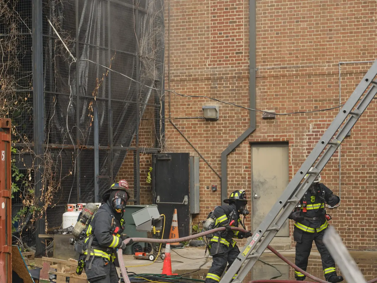 The image shows a group of firefighters wearing helmets and holding pipes in their hands, working...