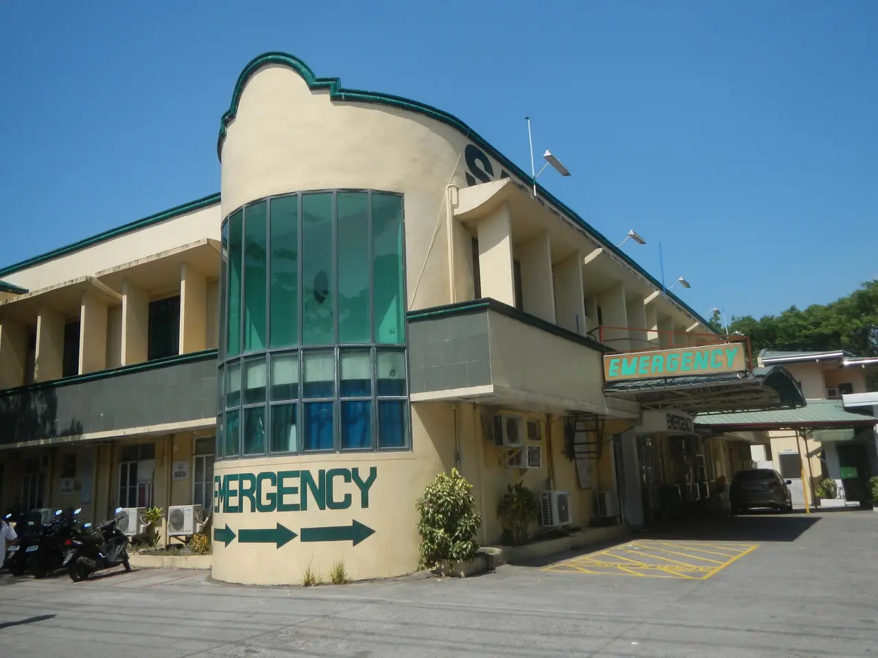 The image shows a building with a sign that reads "Emergency" on the side of it, surrounded by...