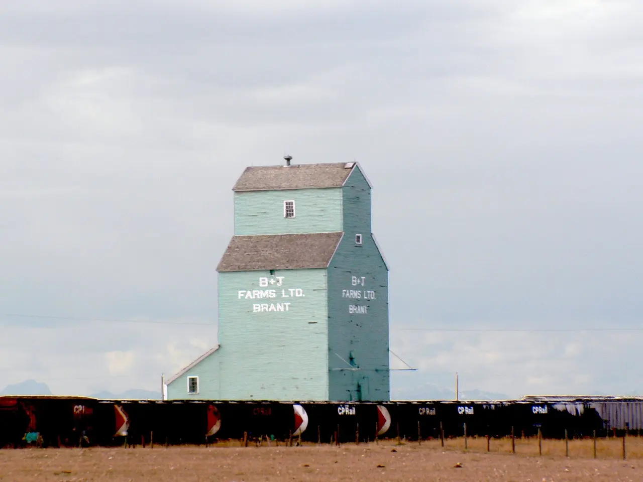 The image shows a grain elevator sitting in the middle of a field, surrounded by a fence. The...