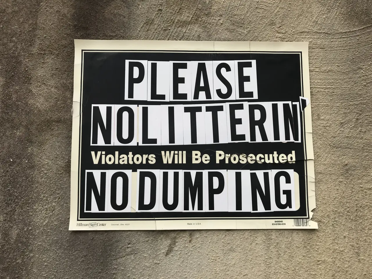 The image shows a black and white sign on the side of a building that reads "Please Nolitterin'...