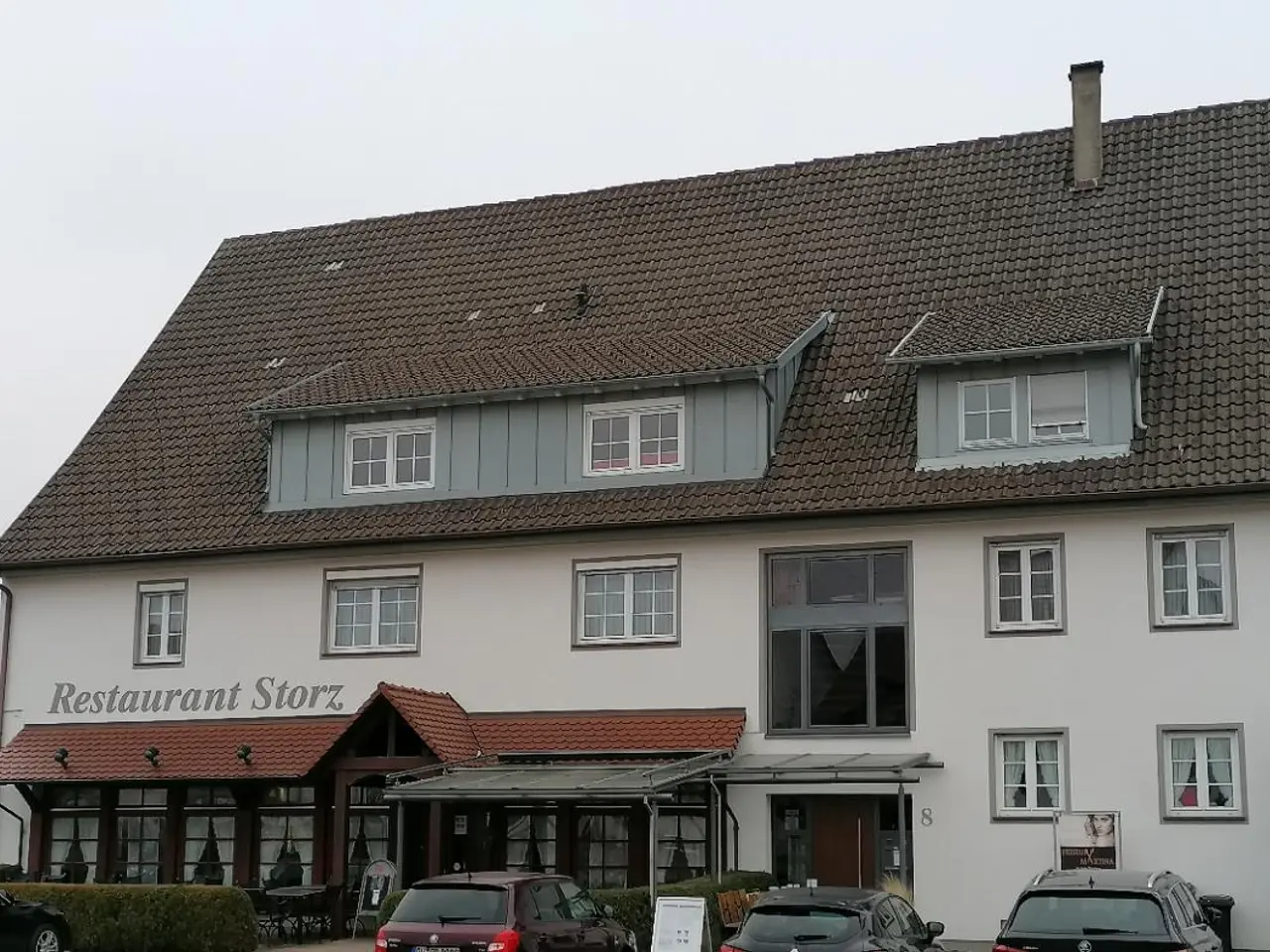 The image shows a restaurant storz in the middle of a parking lot with cars parked in front of it....