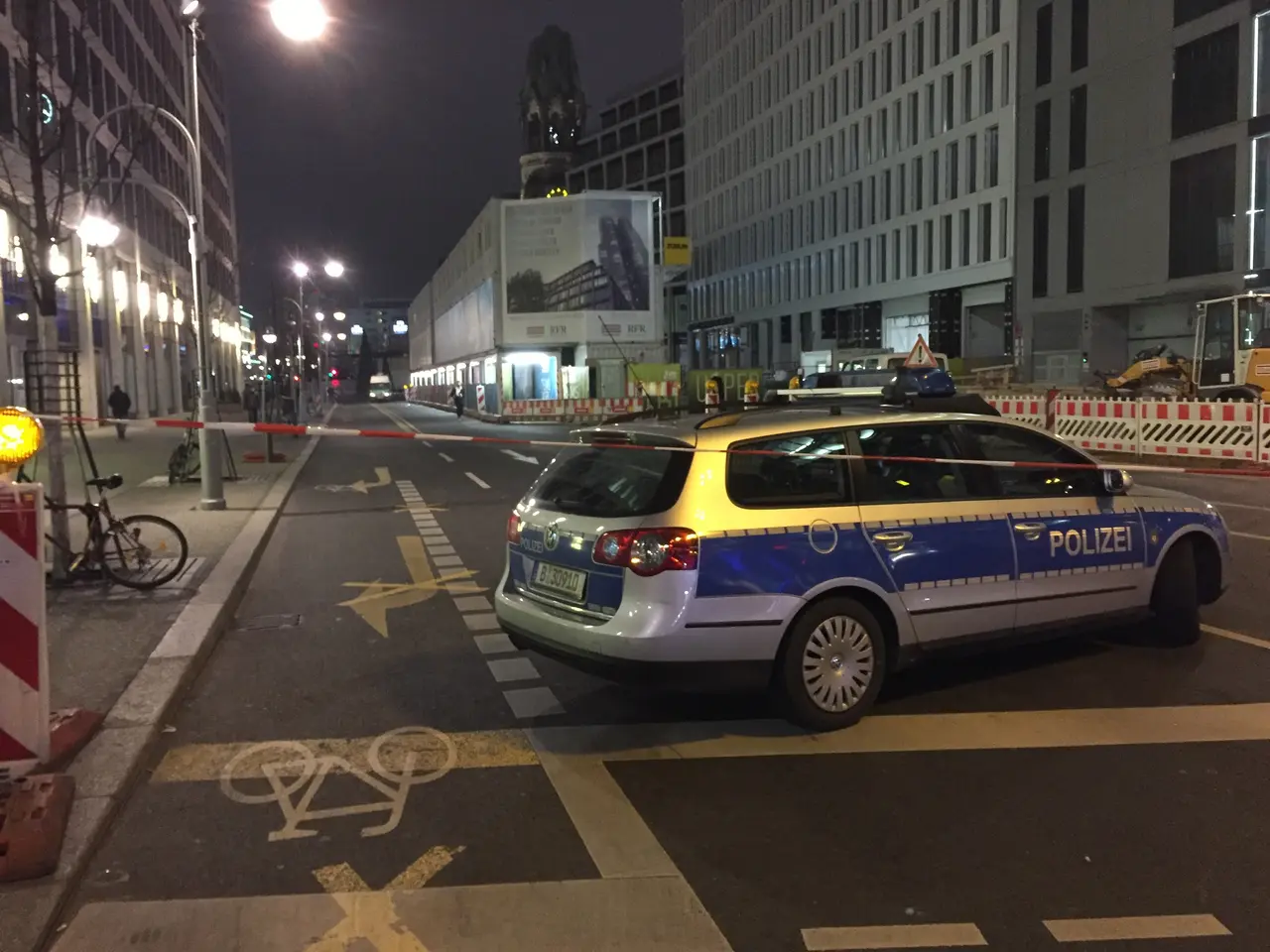 The image shows a police car parked on the side of a street at night, surrounded by buildings,...