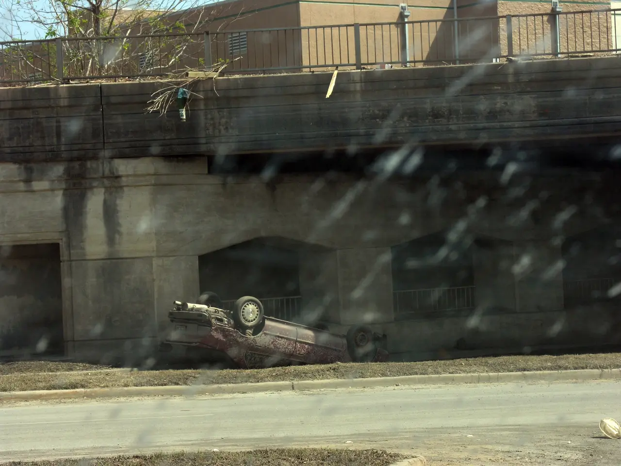 The image shows a car that has crashed into a bridge on the side of the road. The car is surrounded...