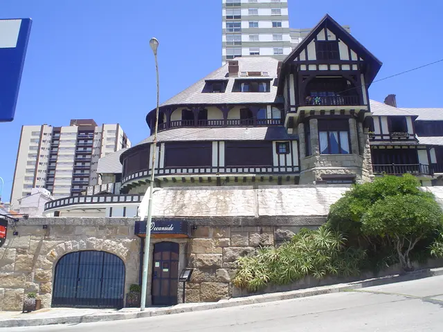 In this picture we can see few buildings, trees, pole and lights, also we can find few hoardings.