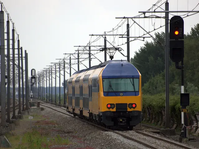 In this image there is a railway track in the middle, on which there is a yellow color train , in...