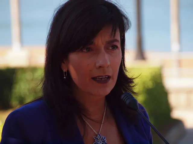 In this image there is a woman. In front of her there is a microphone. Behind her there are plants....