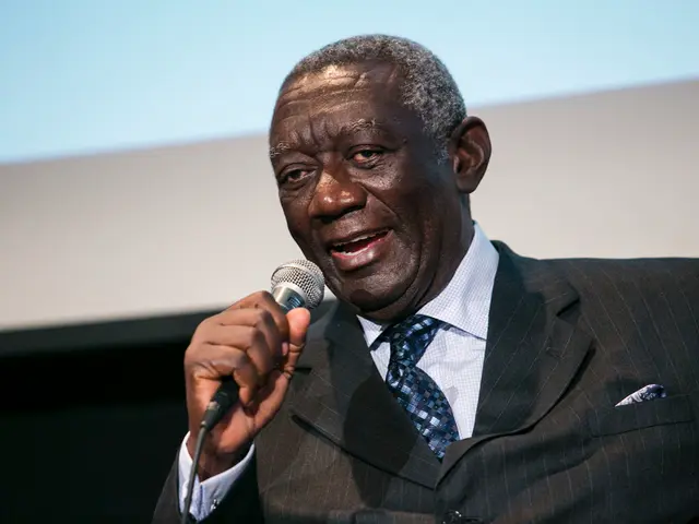 The person wearing black suit is speaking in front of a mic.