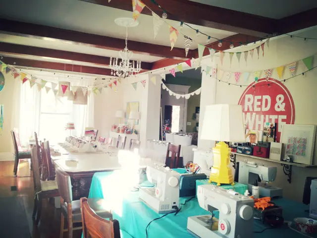 In the image there are sewing machines on a table and behind there is a dining table, on the right...