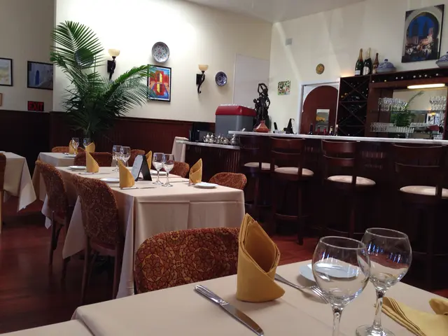 It is a restaurant there are many tables and chairs and on the table there are two glasses,napkins...