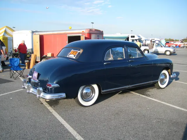 In this picture we can see old black Vintage car on the road. Behind we can see a red color van and...