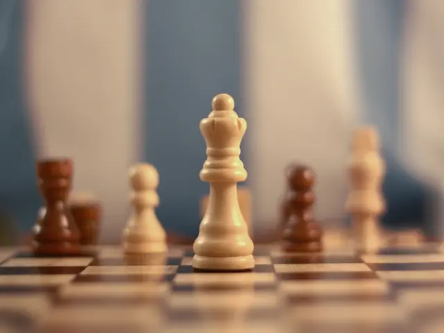 In this image we can see a chess board with chess coins. The background of the image is blur.